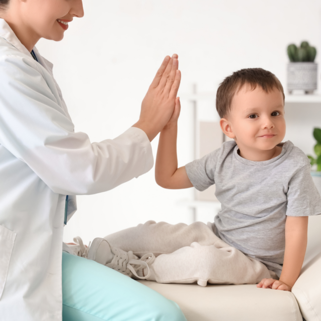 Pediatrician and smiling toddler share a high-five in a bright clinic room, creating a friendly atmosphere.