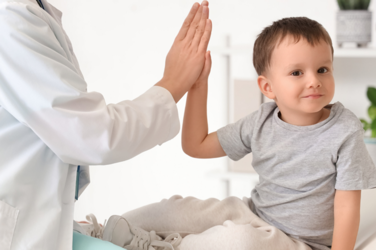 Pediatrician and smiling toddler share a high-five in a bright clinic room, creating a friendly atmosphere.